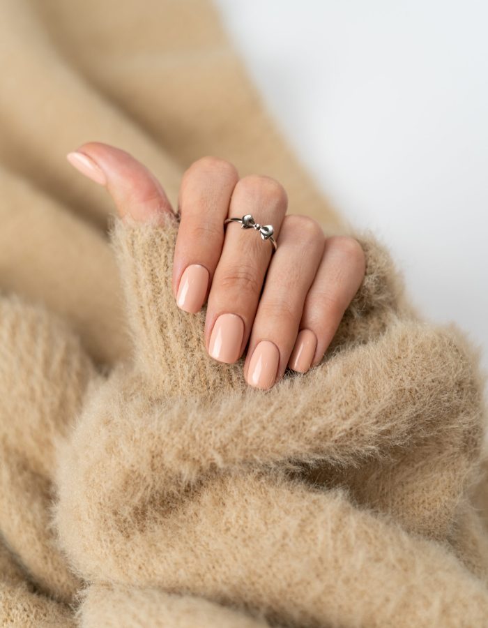 Graceful thin fingers of a girl with a trendy pastel nude manicure and a fluffy soft sweater and a cute silver ring bow